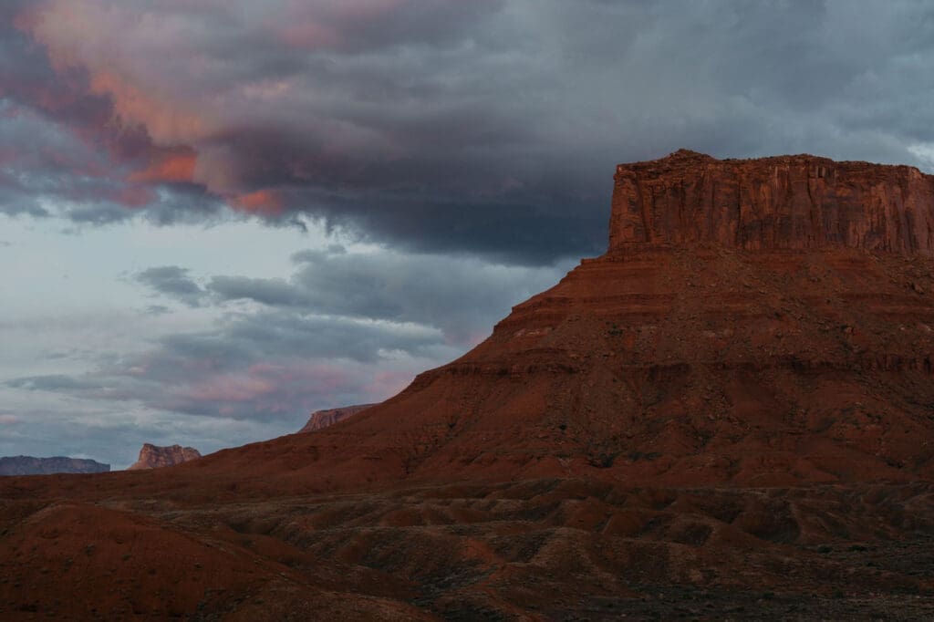 Dramatic red desert mesa under stormy sunset sky, showcasing remote and adventurous elopement location potential.