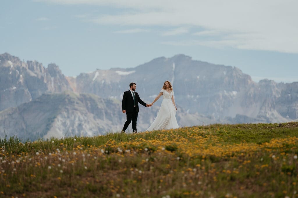 Elopement couple walking across a scenic mountain ridge in Telluride, one of the most breathtaking elopement spots in Colorado.