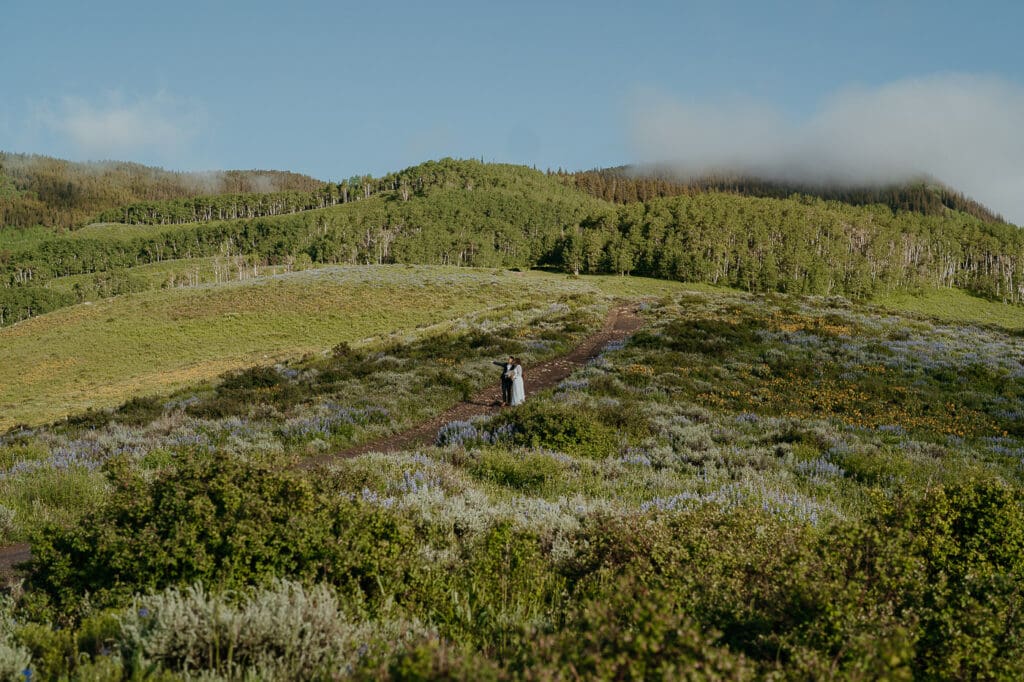Elopement couple standing on a wildflower-lined trail at sunrise in Crested Butte, Colorado.