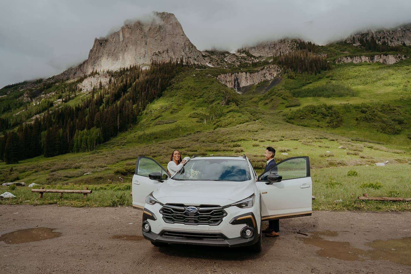 Couple at one of the best elopement spots in Colorado, standing by their car with mountain views and alpine greenery in the background.