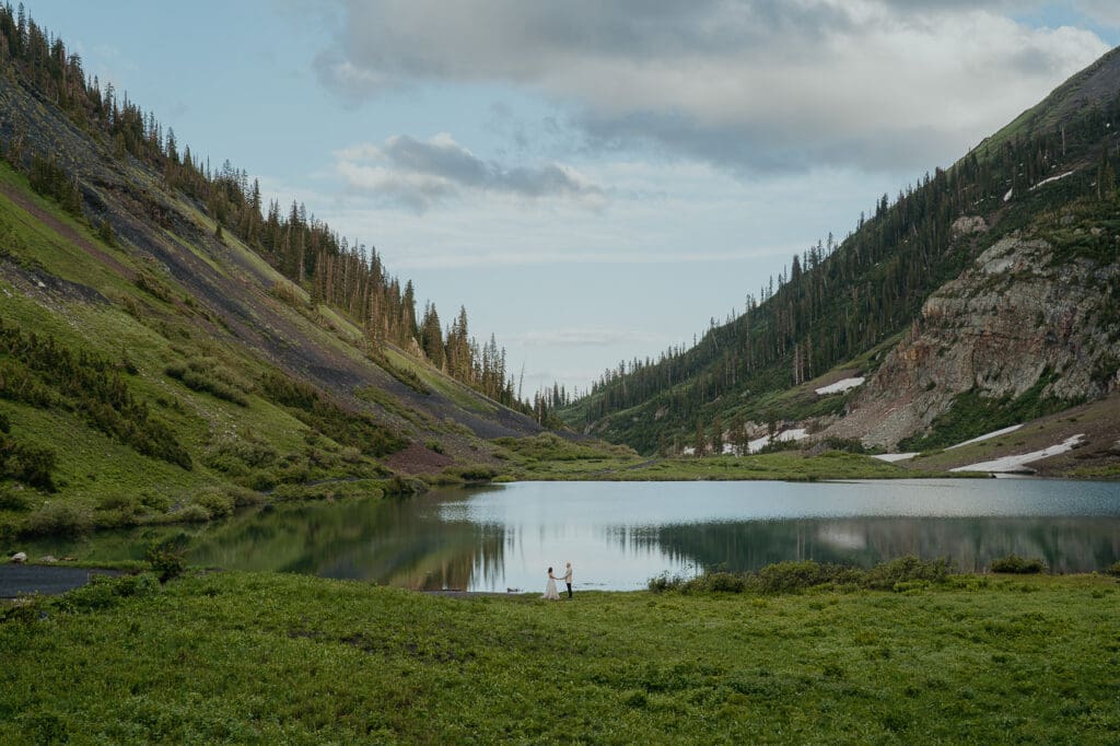 Couple eloping beside an alpine lake surrounded by dramatic mountain cliffs.
