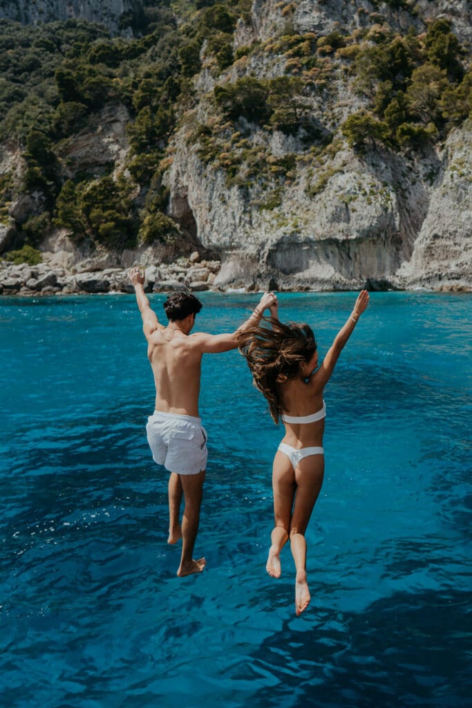A couple jumps into bright blue water hand-in-hand during their adventure elopement, capturing the kind of spontaneous, joy-filled moment that can be part of a full-day elopement timeline.