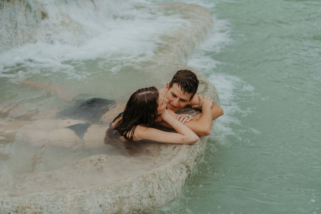 A couple relaxes together in a natural hot spring during their elopement day, showing how an intentional elopement timeline can include slow, meaningful moments like this.